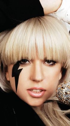 lady with blond hair and black face paint on her face posing for the camera while wearing white gloves