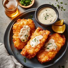 fried food on a plate with dipping sauces and lemon wedges next to it