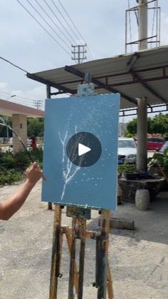 a man is painting on an easel in front of a building with a sky background