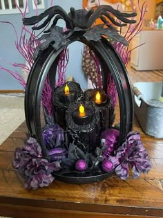 some candles are sitting in a metal frame with purple flowers and branches around it on a wooden table