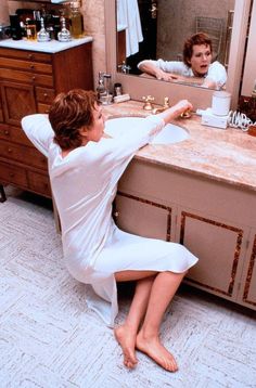 a woman sitting in front of a bathroom mirror