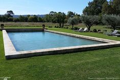 an empty swimming pool in the middle of a grassy field with lounge chairs around it