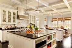 a large kitchen with white cabinets and black counter tops, an island that has fruit on it