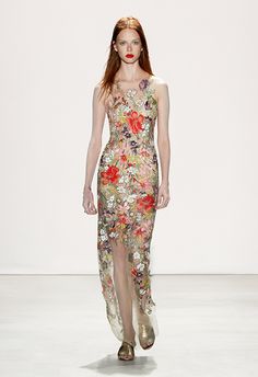 a woman walking down a runway wearing a dress with flowers on it