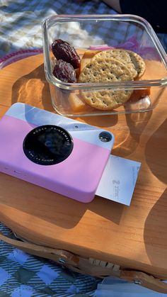 a pink camera sitting on top of a wooden table next to a container of food