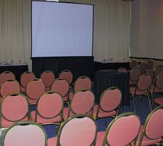 rows of pink chairs in front of a projector screen at a conference or meeting room