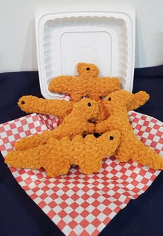 four teddy bears sitting on top of a red and white checkered cloth next to a plastic container