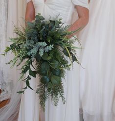 a woman in a white dress holding a bouquet of flowers and greenery next to her wedding gown