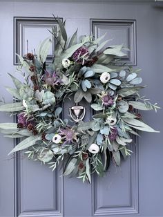 a wreath on the front door with flowers and greenery hanging from it's side