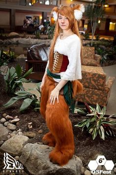 a woman dressed up as a fox standing in the middle of a room with rocks and plants