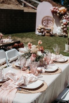 the table is set with pink and white flowers in vases, plates and napkins