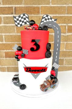 a three tiered cake with cars and race flags on the top is decorated in red, white and black