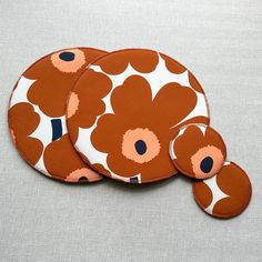 three orange and white flowered coasters sitting on top of a gray tablecloth