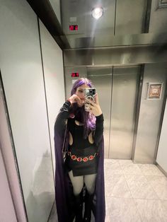 a woman taking a selfie in an elevator with purple hair and black cape on