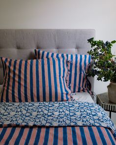 a bed with blue and red striped pillows on it next to a potted plant