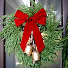 a wreath with bells and a red bow hanging from the front door, next to evergreen branches