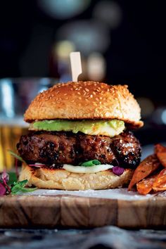 a hamburger with meat, lettuce and cheese on it next to sweet potato fries