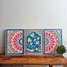 three paintings are sitting on top of a wooden table next to a plant and potted plant