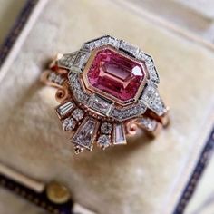 a pink diamond ring sitting on top of a white cushioned box with gold trimmings