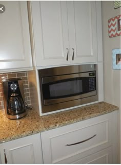 a stainless steel microwave oven sitting on top of a kitchen counter next to white cabinets