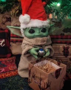 a star wars baby yoda in a santa hat holding a christmas ornament