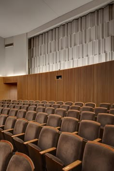 an empty auditorium filled with brown chairs and wooden paneling on the wall behind it