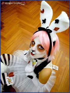 a woman dressed in bunny ears and white dress with pink hair is posing for the camera