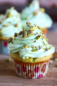 cupcakes with white frosting and pistachio toppings on wooden table