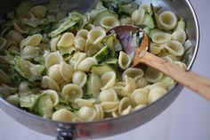 a pot filled with pasta and vegetables being stirred by a wooden spoon