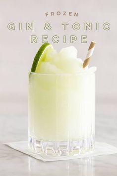 a glass filled with ice and lime on top of a white table next to a wooden spoon