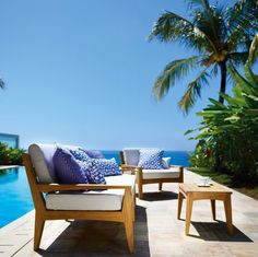 two wooden chairs sitting next to each other on top of a tiled floor near a swimming pool