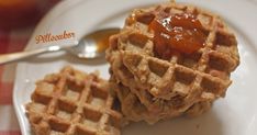 two waffles on a white plate with syrup and a spoon in the background