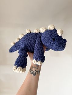 a hand holding up a crocheted blue dinosaur toy with white tusks