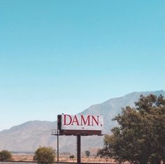 there is a large sign that says damn on the side of a road in front of mountains