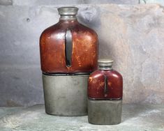 two metal containers sitting next to each other on top of a stone surface with rocks in the background