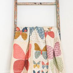 an old ladder is hanging on the wall next to a quilted piece of cloth