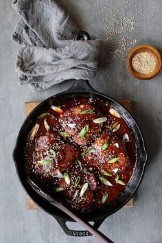 an iron skillet with meat and vegetables in it next to a bowl of seasoning