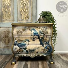 a blue and white bird painted on an old dresser with gold trim, sits next to a potted plant