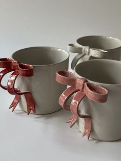 three white cups with pink bows on them