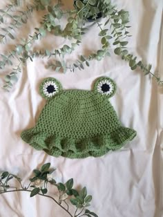 a green crocheted frog hat with eyes on it's head and leaves in the background