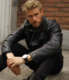 a man sitting on the ground wearing a black leather jacket and white watch with his hands crossed