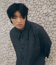 a young man with black and white striped shirt standing in front of a rock wall