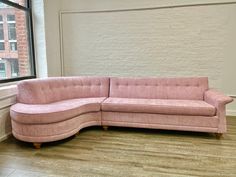 a pink couch sitting in front of a window on top of a hard wood floor