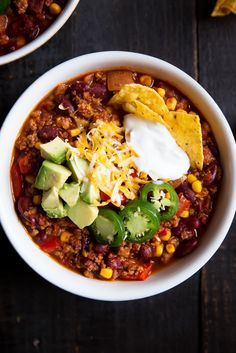 two bowls filled with chili, corn and avocado