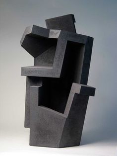 an abstract concrete sculpture sitting on top of a white table next to a gray wall