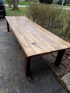 a wooden table sitting on the side of a road next to a parked car and bushes