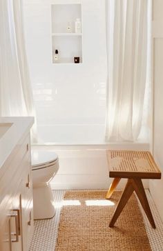 a white bathroom with a wooden bench in front of the toilet and shower curtained window