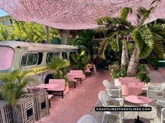 an outdoor dining area with tables, chairs and a van covered in pink paper flowers