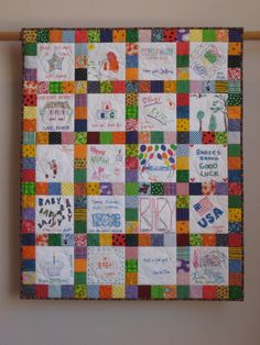 a multicolored quilt hanging on the wall with words and pictures written on it