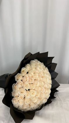 a bouquet of white roses sitting on top of a black wrapper in front of a white backdrop